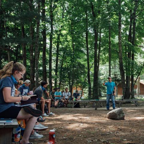 An outdoor meeting of young people with a man standing and speaking