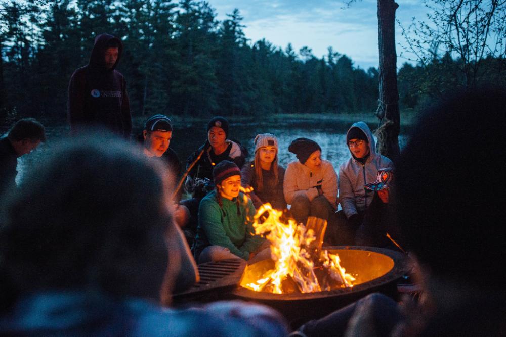 People sitting around campfire at night at HoneyRock in Three Lakes, WI