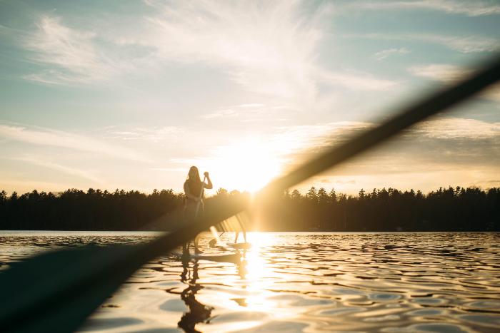 students paddleboarding on Long Lake at HoneyRock as the sun sets