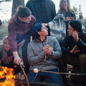 students gather around a fire and roast marshmallows at HoneyRock in three lakes, wi