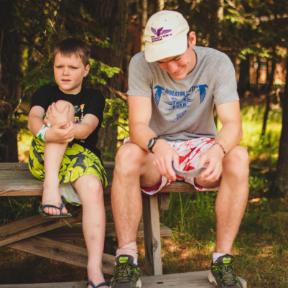 counselor talks with camper on a bench at HoneyRock in Three Lakes, WI