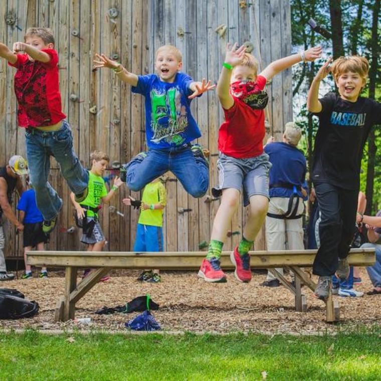 young camper boys jumping off a bench at the rock wall