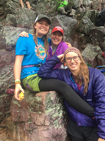 3 students smiling while sitting on rocks