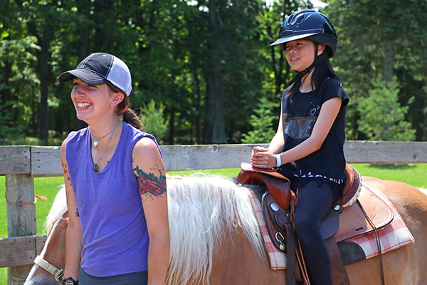 Girl riding a horse while instructor smiles