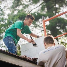 HoneyRock staff paint a chimney on top of a cabin in Three Lakes, WI